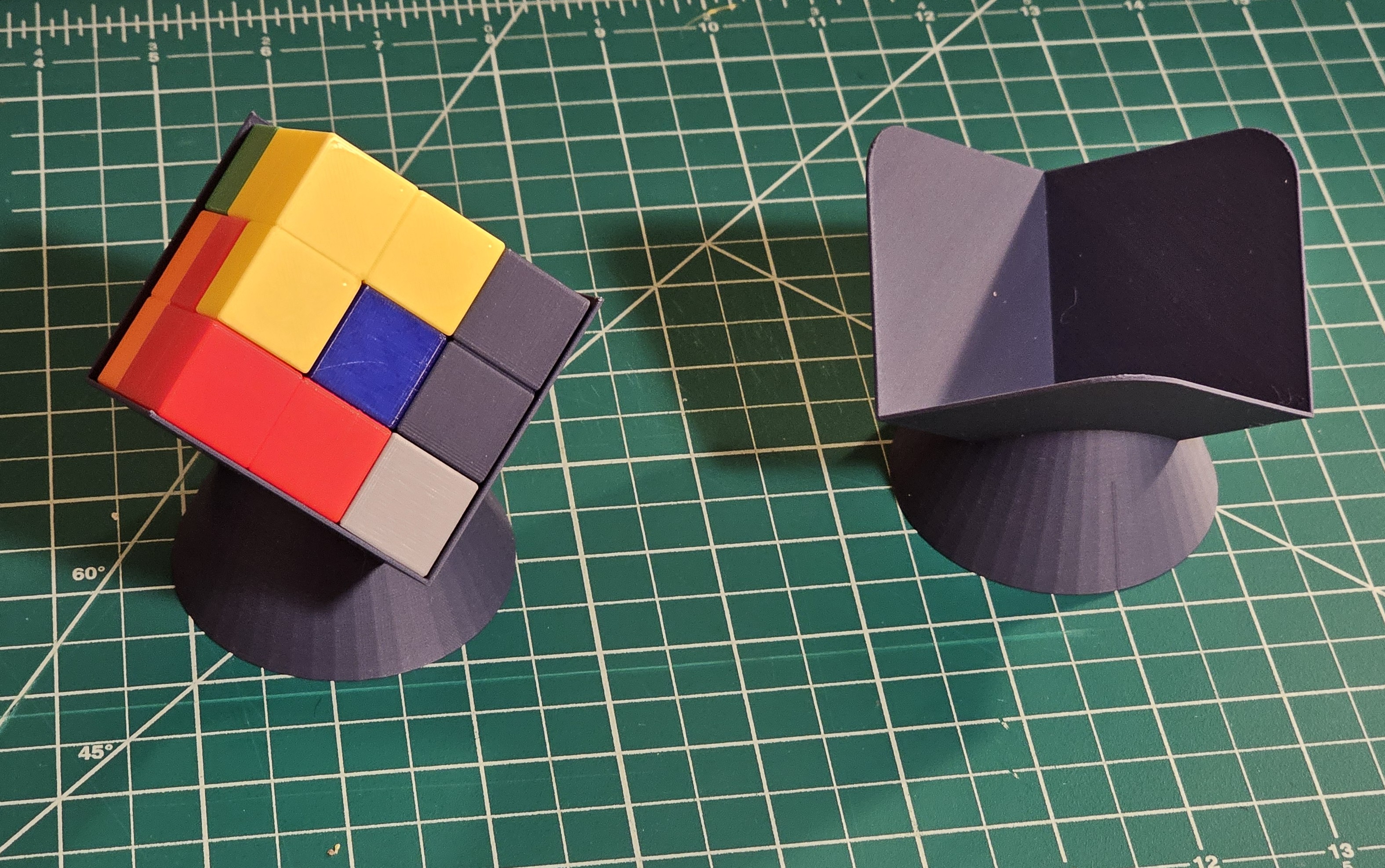 A set of 3D-printed Soma cube pieces in several colors, assembled into and arranged around a 3×3×3 cube.