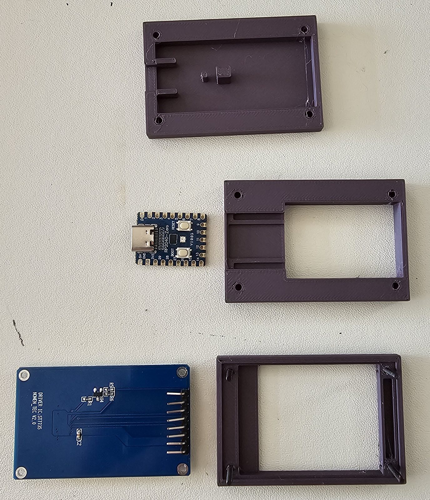 Three printed enclosure layers laid out beside a Waveshare RP2040-Zero board and the back of the ST7735 display module.